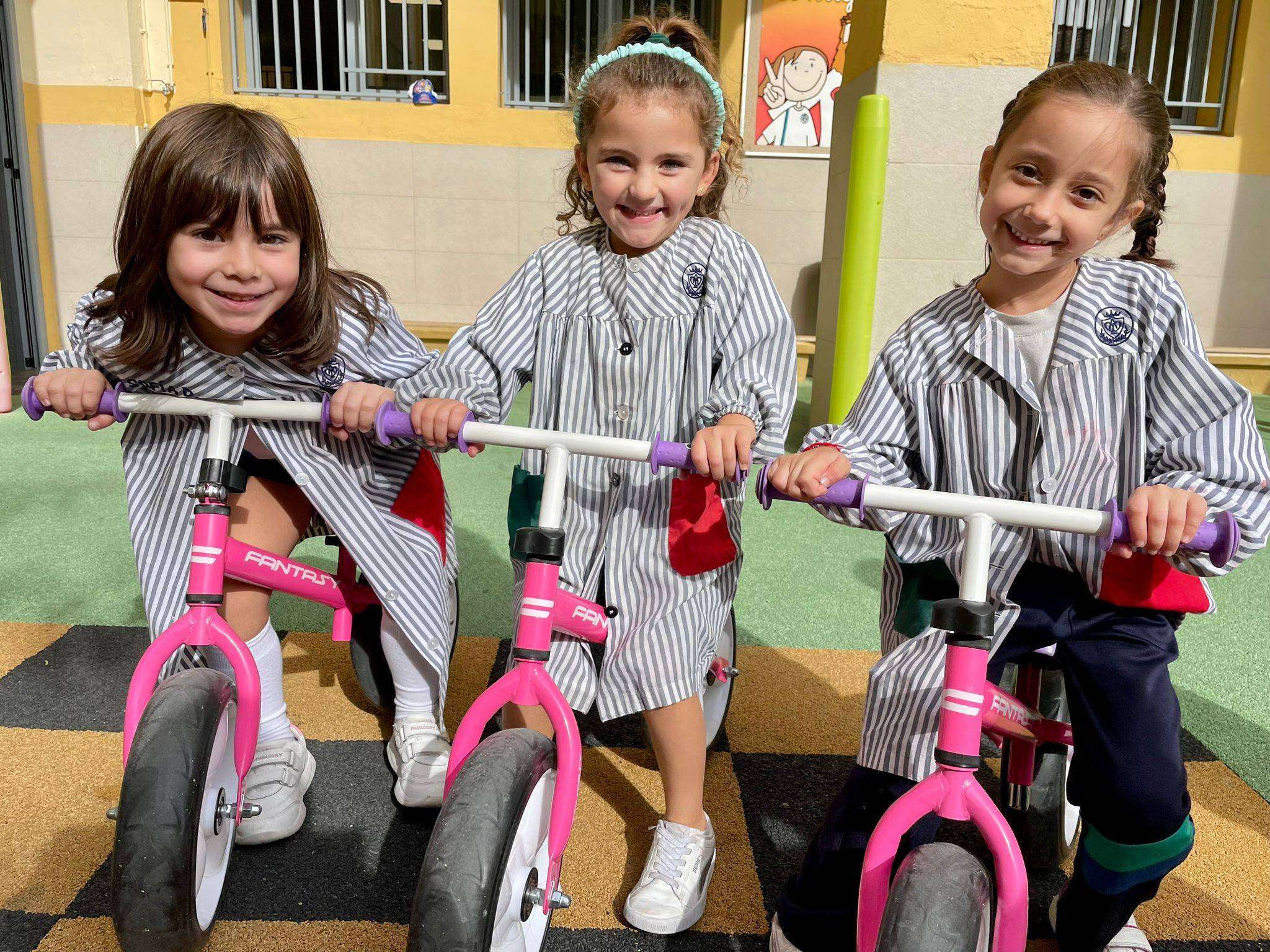 Tres alumnas del colegio Pureza de María Grao con babero , subidas a tres bicicletas rojas.