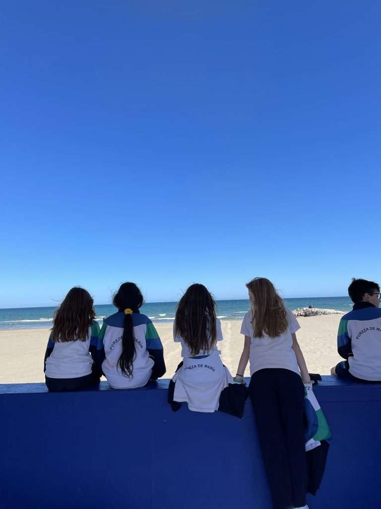 Cuatro alumnas y un alumno de Pureza de María Grao sentados en un muro mirando al mar.